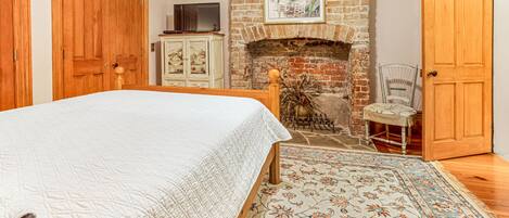 A bedroom with a bed, a fireplace, a wooden wardrobe, and a television on a cabinet.