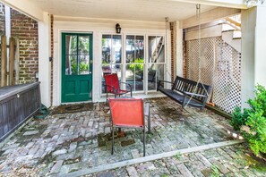 A covered patio with a brick floor, a green door, and outdoor seating including a red chair and a bench.