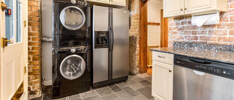 A kitchen with a brick wall, a stainless steel refrigerator, a dishwasher, and a washing machine.
