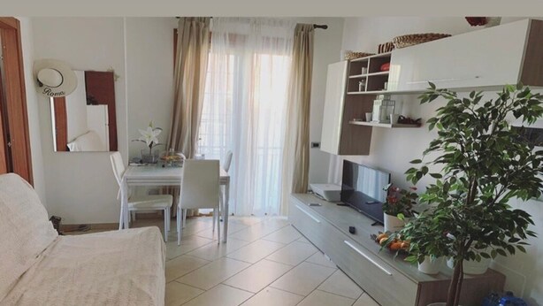 A living room with a sofa, a dining table with chairs, a TV, and a potted plant. - Extraordinary vacations (Villa Verde)