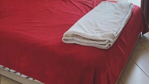 A single bed with a red bedspread and a white towel, a red pillow, and a curtain partially drawn to the side. - Extraordinary vacations (Villa Verde)