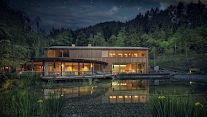A modern house with a wooden exterior, large windows, and a dock extending into a pond. - Naturhotel Saalerwirt (San Lorenzo di Sebato)