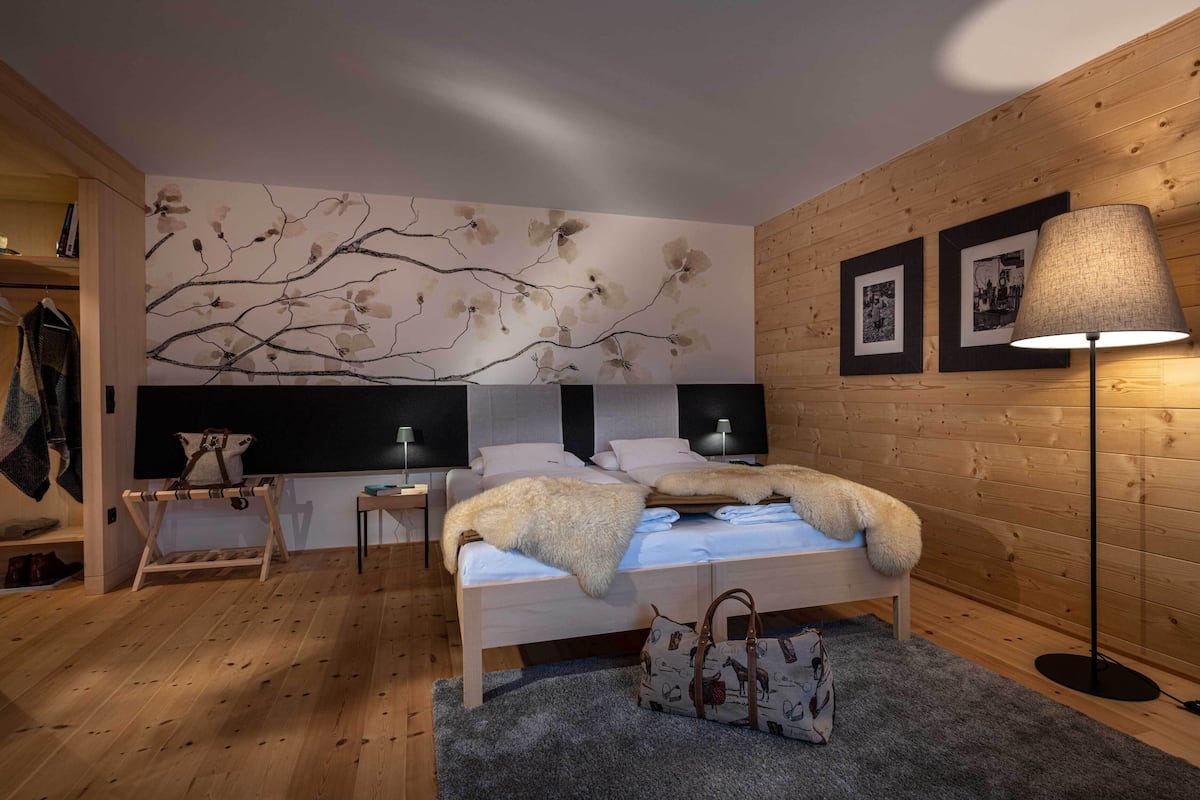 Een moderne slaapkamer met een houten vloer, een bed met een zachte deken, een staande lamp en een kunstwerk aan de muur.