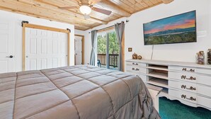 Ein Schlafzimmer mit Bett, Kommode, Fernseher und Blick ins Freie.
