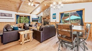 Ein gemütliches Blockhaus-Interieur mit Kamin aus Stein, Holzboden und einem Essbereich mit Metallstühlen.