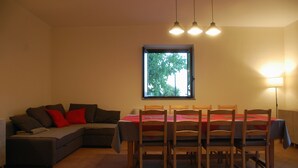 En matplats med ett bord för fyra personer, en soffa och ett fönster med utsikt över träd.