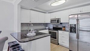 Une cuisine moderne avec des meubles blancs, un plan de travail noir, un réfrigérateur en acier inoxydable, un four à micro-ondes et une cuisinière.