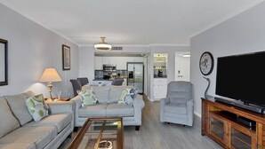 Un salon moderne avec un canapé gris, un fauteuil gris, une table basse et un téléviseur à écran plat posé sur un meuble en bois.