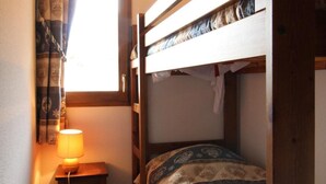 A small, cozy room with a bunk bed, a bedside table with a lamp, and a window with patterned curtains. - 10m from resort center, 2nd floor, balcony, tv, ski locker, 42m², Aussois (Aussois)