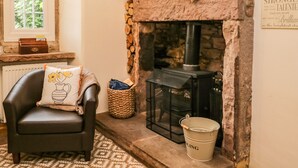 A cozy room with a stone fireplace, a leather chair with a decorative pillow, a wicker basket, and a bucket. - The Lodge (Penrith)