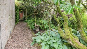 A stone building with a gravel path leading to a wooden door. - The Lodge (Penrith)