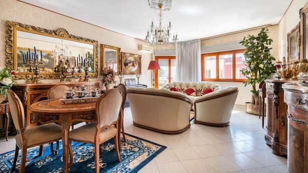 A spacious living room with a round coffee table, two armchairs, a sofa, and a chandelier.