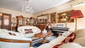 A spacious living room with a chandelier, white leather sofas, a coffee table, and a piano.
