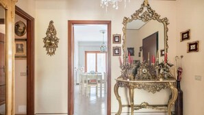 A hallway with a grand mirror, a chandelier, and a dining area in the background.