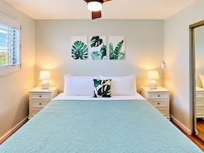 A bedroom with a bed, two bedside tables, a ceiling fan, and wall art.