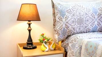 A neatly made bed with patterned bedding, a bedside lamp, and a small decorative plant on a wooden nightstand.
