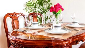 Une table à manger dressée avec des assiettes, des couverts et des verres, entourée de chaises et agrémentée d’un vase de fleurs.