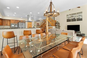Une cuisine moderne dotée d’appareils électroménagers en acier inoxydable, d’une table à manger en verre et d’un escalier menant à une mezzanine.