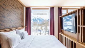 A hotel room with a large bed, a TV mounted on the wall, and a balcony with a mountain view.