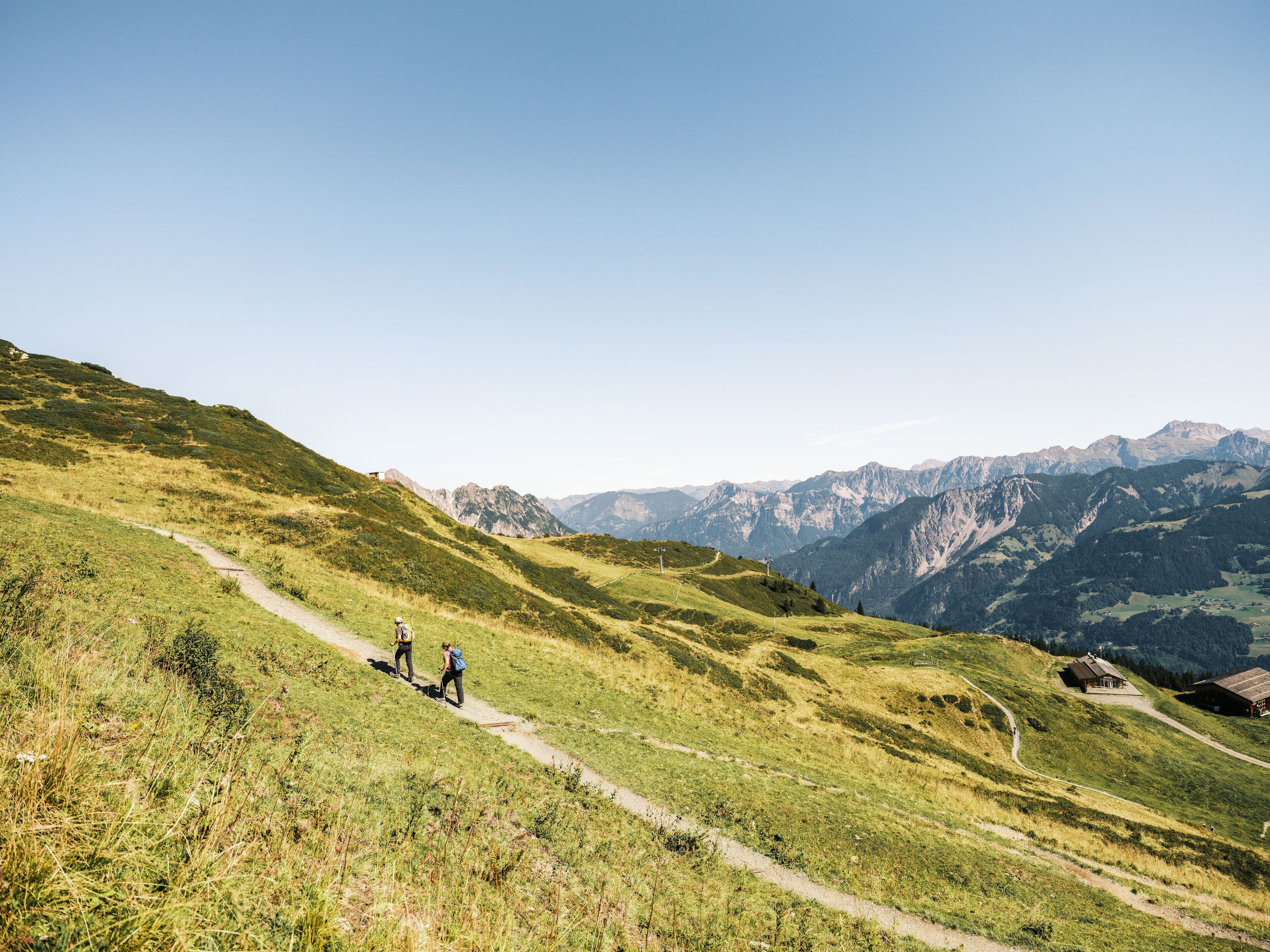 A hiking trail on a grassy hillside with a mountain range in the background.