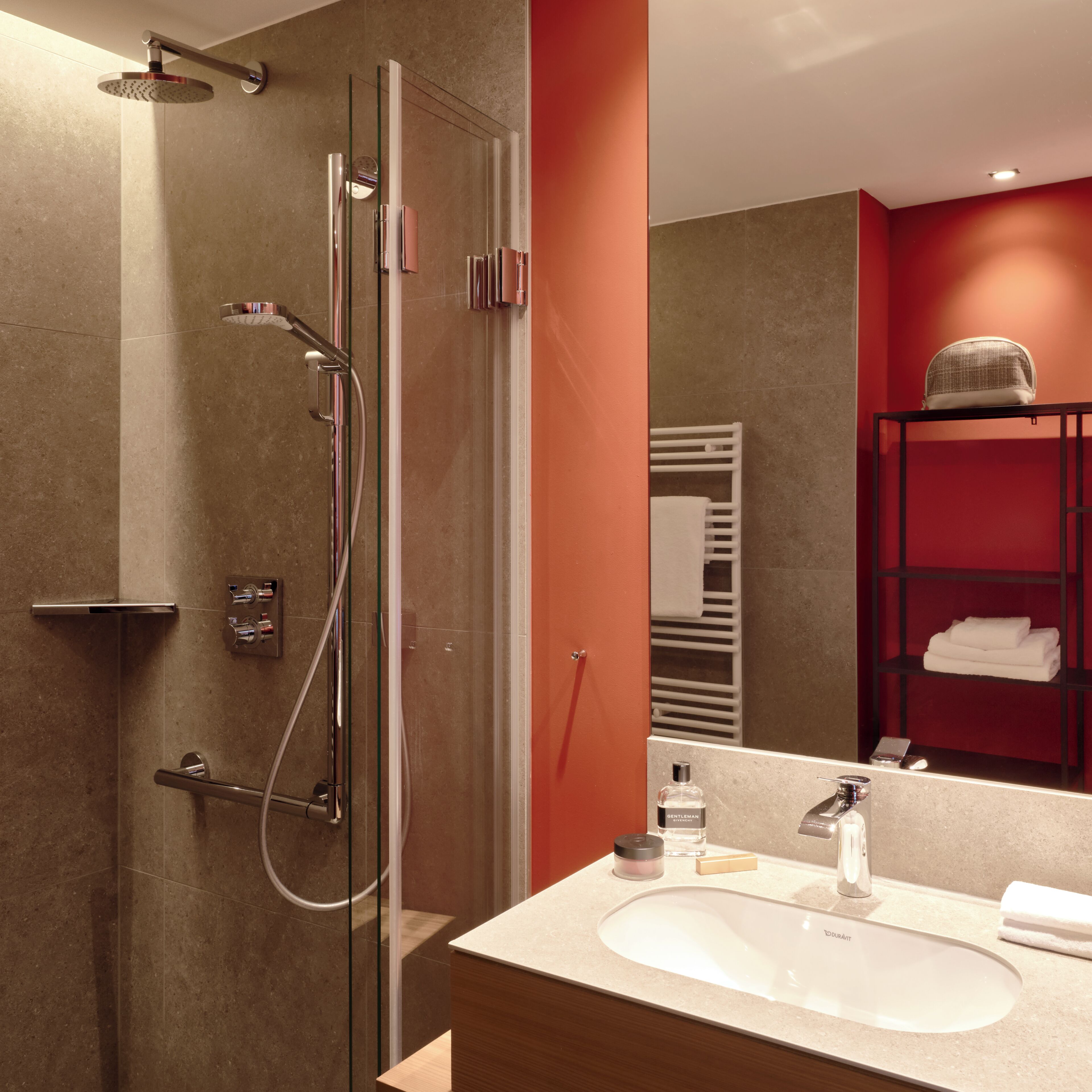 A modern bathroom with a glass-enclosed shower, a white sink, and a red shelving unit in the background.