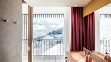 Ein modernes Badezimmer mit großem Fenster, einem Balkon und Blick auf schneebedeckte Berge.