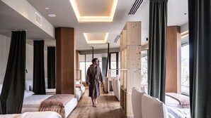Una habitación de hotel moderna con piso de madera, ventanas amplias y un pasillo central.