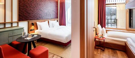 Una habitación de hotel con una cama, una mesita con una lámpara, un sofá rojo y una ventana con cortinas.