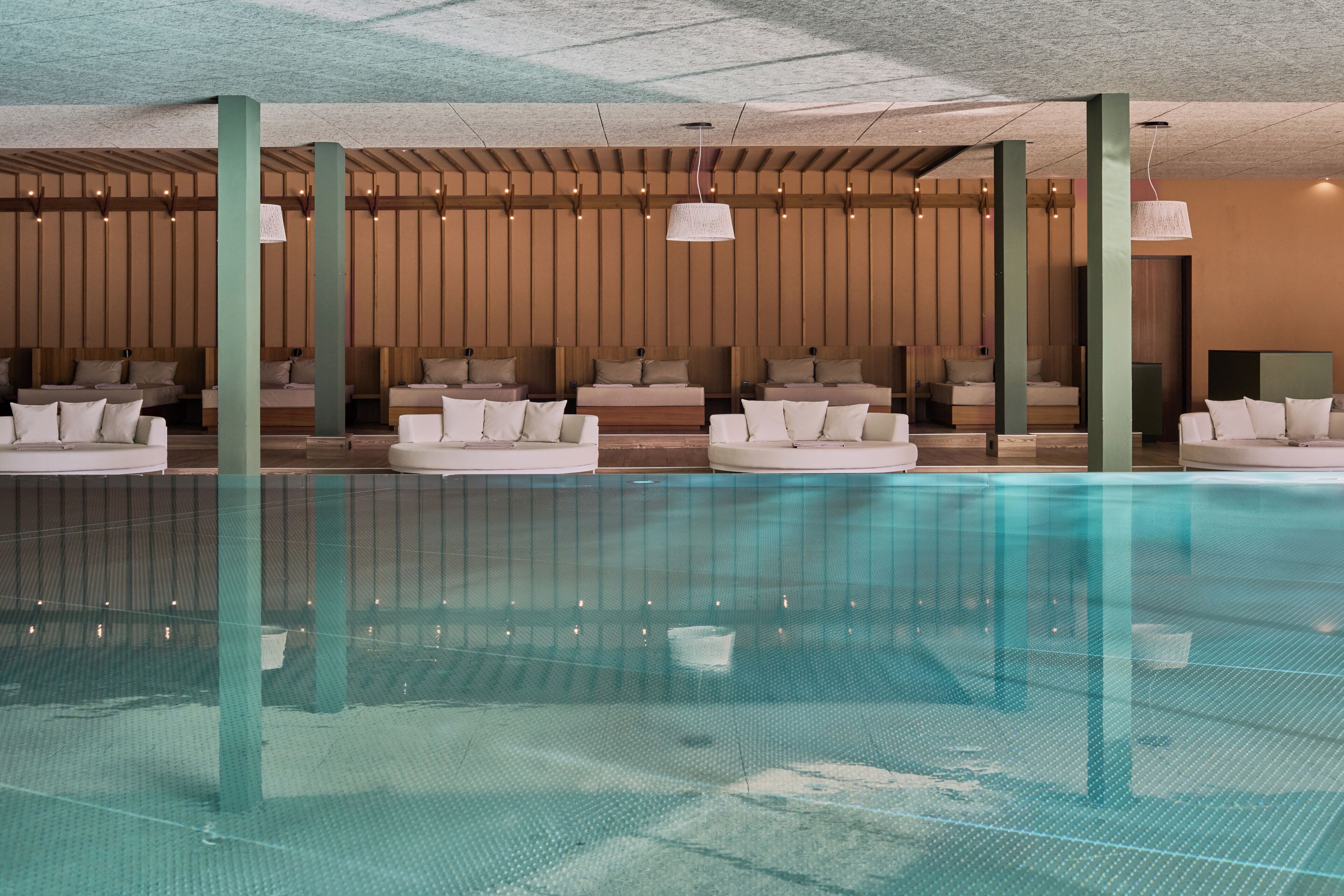 Ein moderner, überdachter Poolraum mit mehreren Liegebereichen und Sitzgelegenheiten.