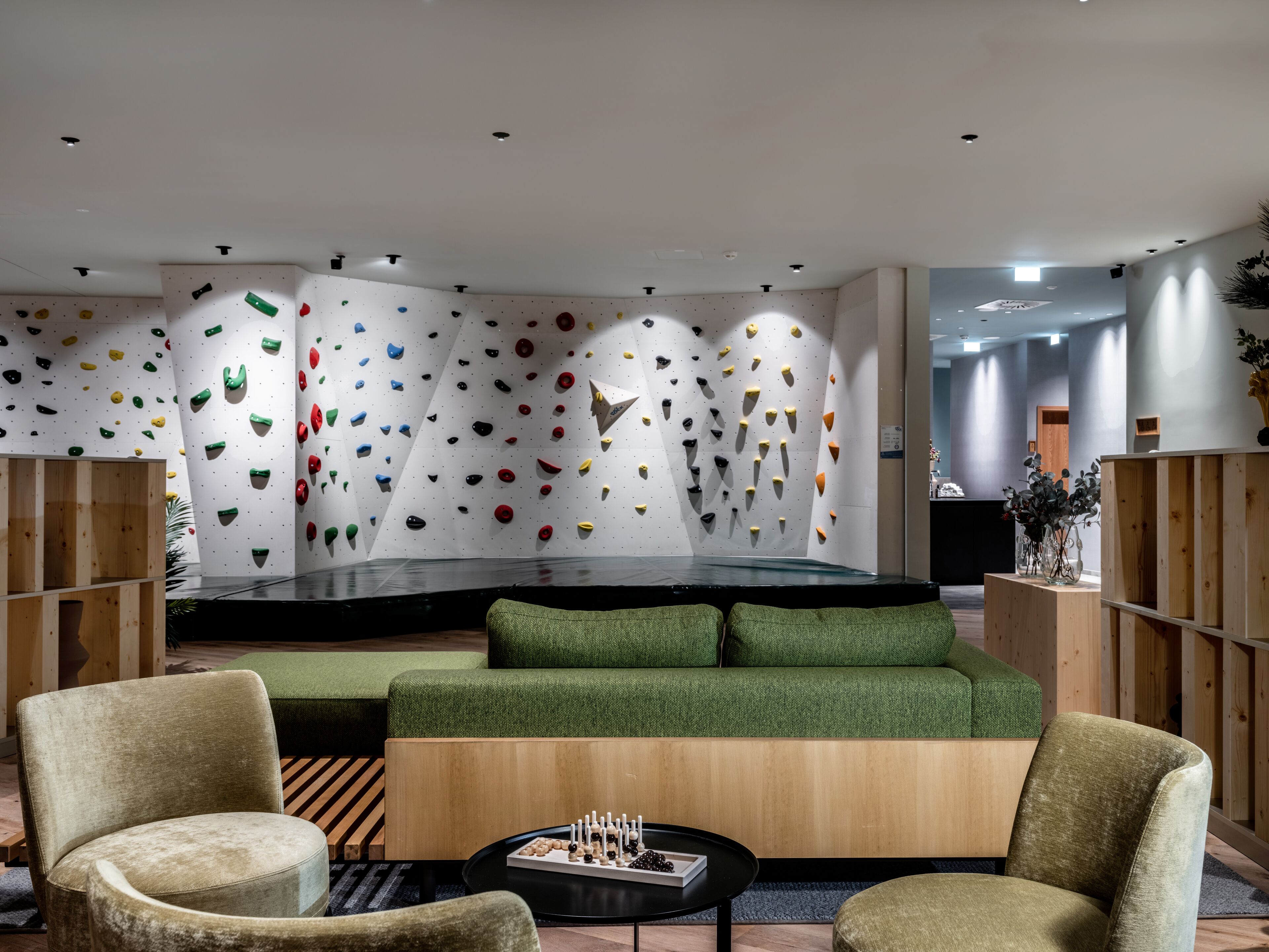 Eine moderne Lobby mit Kletterwänden, grünen Sofas, Holzmöbeln und einem schwarzen Couchtisch.