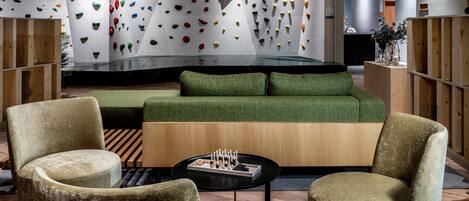 Eine moderne Lobby mit Kletterwänden, grünen Sofas, Holzmöbeln und einem schwarzen Couchtisch.