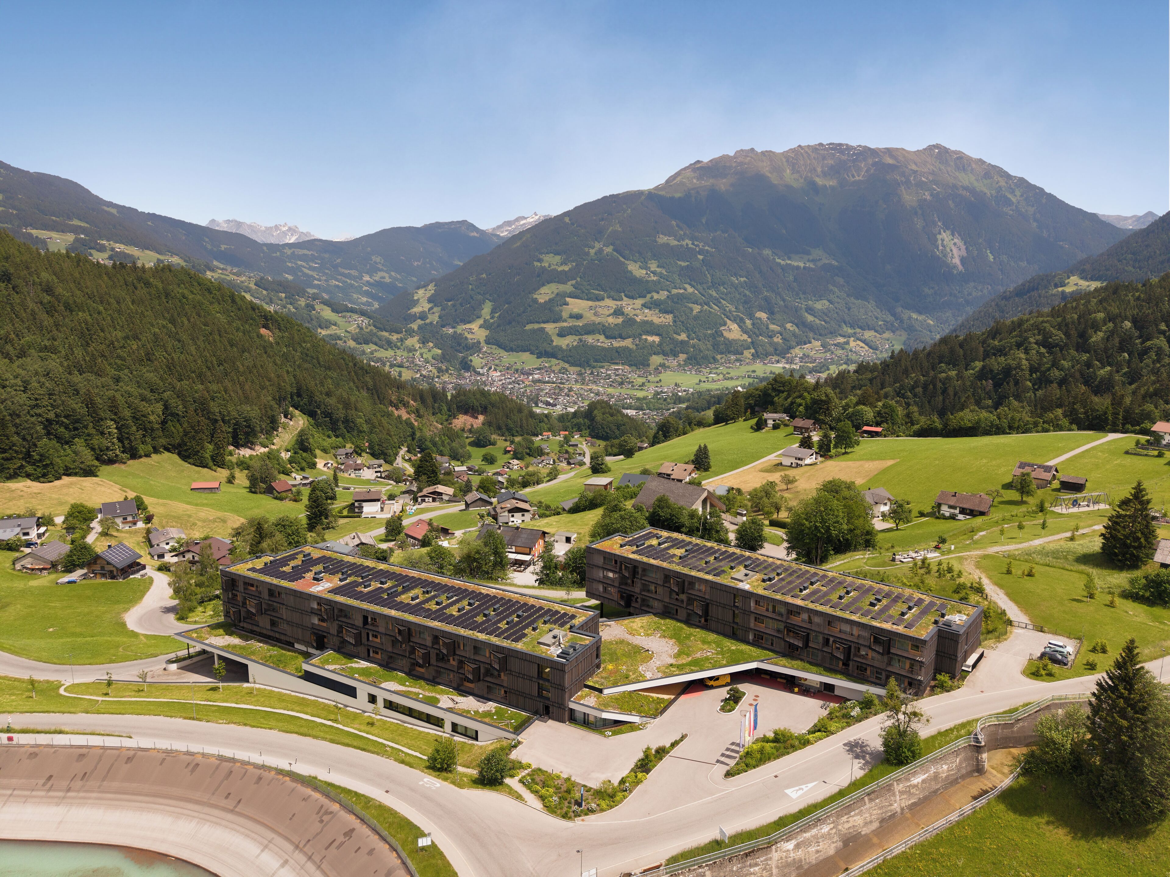 A modern building complex with a parking area and a view of a mountainous landscape.