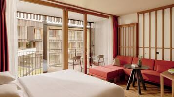 Ein Hotelzimmer mit einem großen Bett, einem roten Sofa, einem kleinen Tisch und Blick auf den Balkon.