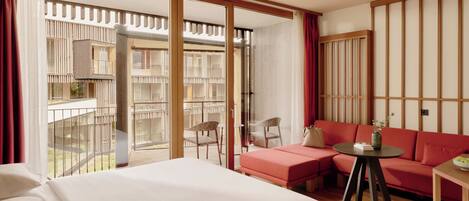 A hotel room with a large bed, a red sofa, a small table, and a view of the outdoor balcony.