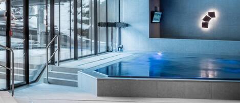 A modern indoor swimming pool with glass walls, a digital display, and a minimalist design.