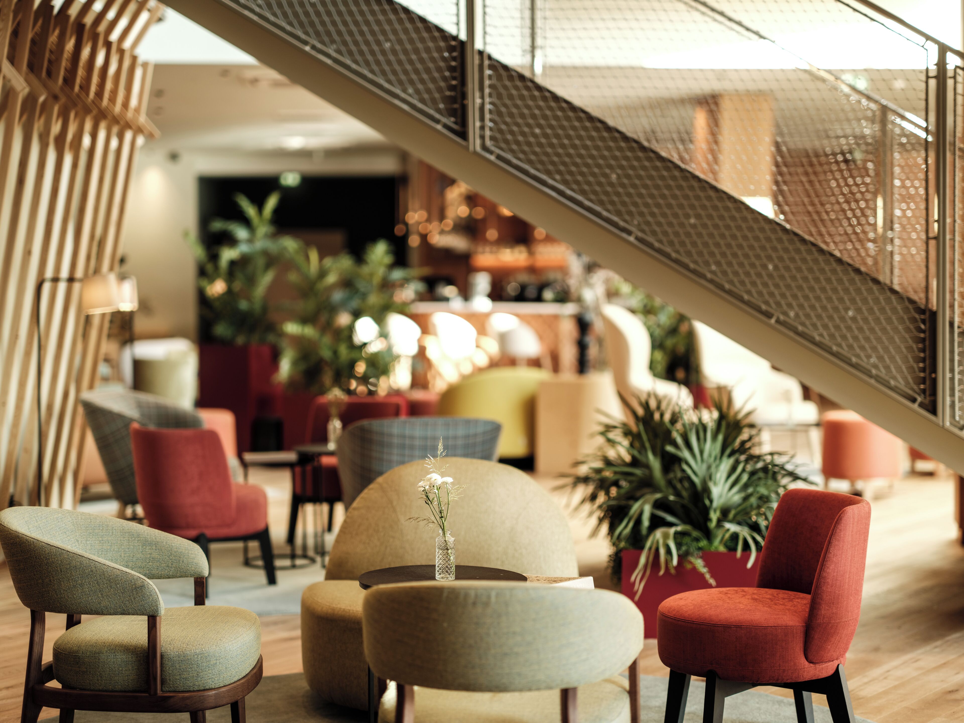 A modern interior with a staircase, seating areas, and indoor plants.