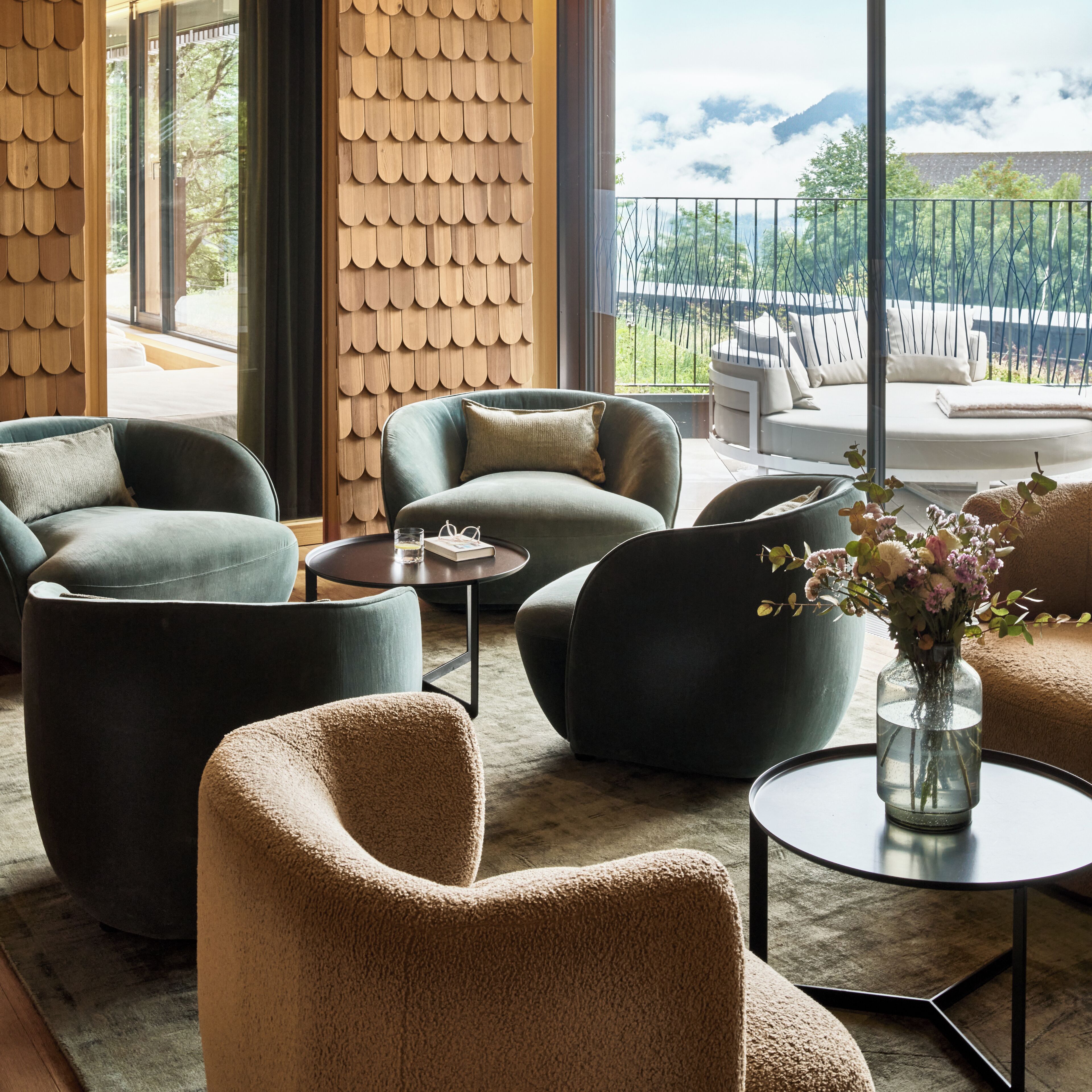Una sala de estar moderna con un ventanal grande, un elemento decorativo de madera y un balcón con mobiliario exterior.