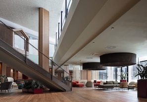 A spacious lobby with a staircase, seating area, and large windows.