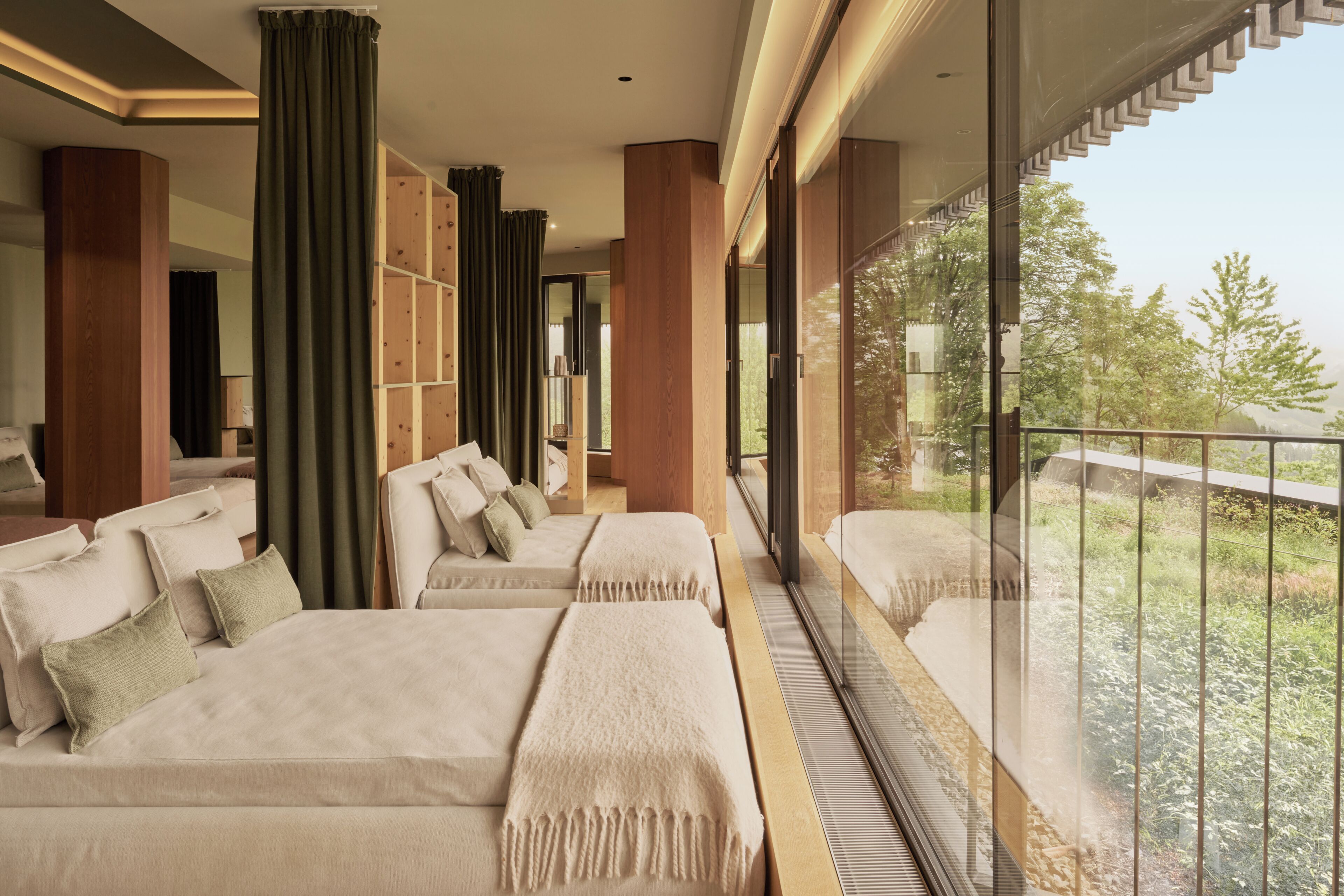 A modern hotel room with a balcony, large windows, and a sofa with multiple pillows.