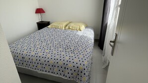 A small, clean room with a bed, a nightstand, a red lamp, and a door with a curtain.