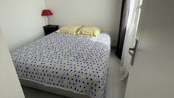 Een kleine, schone kamer met een bed, een nachtkastje, een rode lamp en een deur met gordijn.