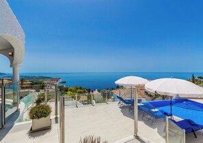 A rooftop pool area with blue lounge chairs and white umbrellas, overlooking a coastal view. - Villa La Palmera with private pool and fantastic views (Salobreña)