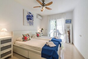 A hotel room with two beds, a ceiling fan, an air conditioning unit, a window with sheer curtains, and a painting on the wall. - Villa La Palmera with private pool and fantastic views (Salobreña)