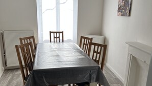 Een eetkamer met een rechthoekige tafel, zes houten stoelen, een radiator, een klok en een raam met gordijnen.