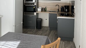 Een compacte keuken met grijze kastjes, een magnetron, een oven, een spoelbak en een koffiezetapparaat.