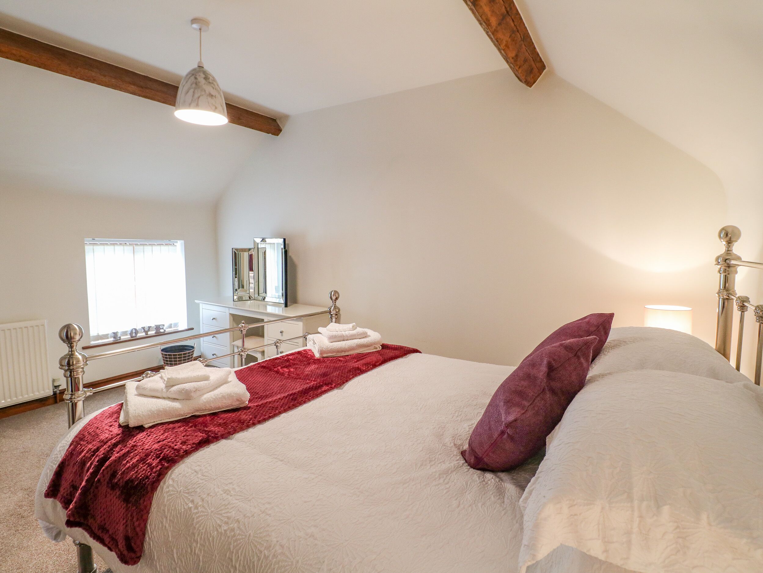 Een slaapkamer met een groot bed, een rode plaid en een houten balk in het plafond.