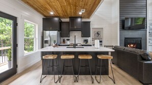 A modern kitchen with a central island, bar stools, a fireplace, and a TV mounted above it. - Relax and Unwind, Hot Tub Under the Stars, Firepit, Sleeps 8 (broken bow)
