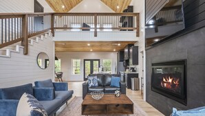A spacious living area with a fireplace, a staircase to an upper level, and a kitchen area. - Relax and Unwind, Hot Tub Under the Stars, Firepit, Sleeps 8 (broken bow)