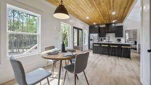 A modern kitchen with wooden ceiling, large windows, and a dining area with a round table and chairs. - Relax and Unwind, Hot Tub Under the Stars, Firepit, Sleeps 8 (broken bow)