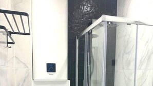 Une salle de bain moderne avec une douche à parois de verre, des toilettes et une poubelle.
